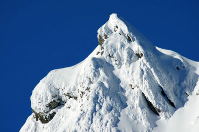 Low angle view of snowcapped mountains against clear blue sky