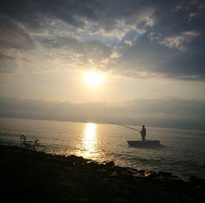 Silhouette man on sea against sky during sunset