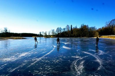 People walking on frozen lake against clear blue sky