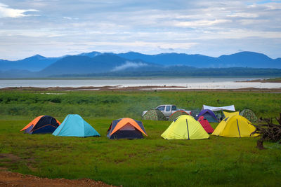 Multi colored tent on field by lake against sky