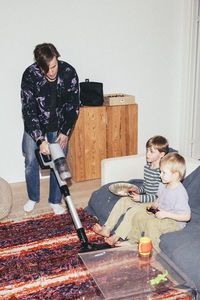 Father vacuuming floor while sons playing video game at home