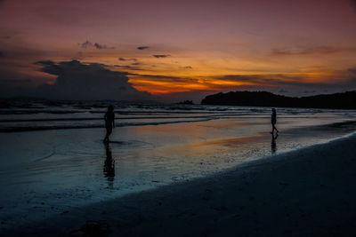 Silhouette people on beach against sky during sunset