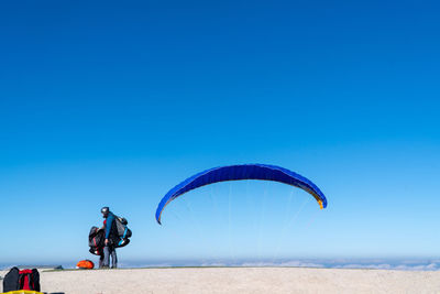 Side view of person standing by parachute against blue sky during sunny day