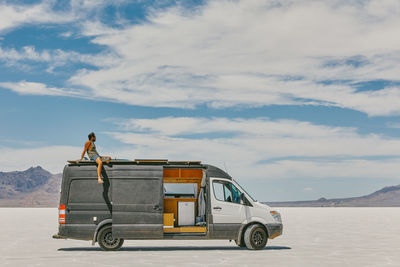 Young man sitting on roof of camper van in bonneville salt flats.