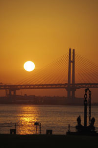 Silhouette bridge over sea against orange sky