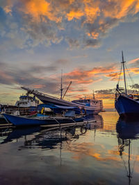 Boats moored in harbor at sunset