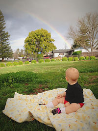 Rear view of boy on field by trees against sky