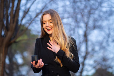 Young woman using phone while standing on tree