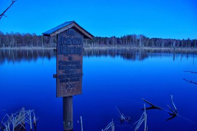 Information sign by calm lake against clear blue sky