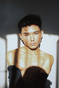 Portrait of shirtless young man against wall at home