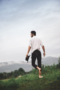 Full length rear view of young man walking on grassy field against sky