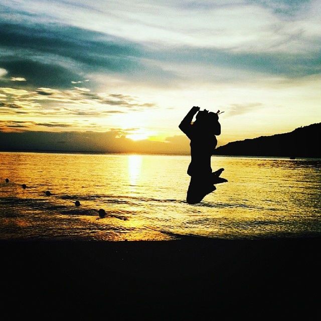 sunset, silhouette, water, sky, sea, lifestyles, leisure activity, scenics, orange color, beach, tranquil scene, beauty in nature, standing, tranquility, shore, cloud - sky, idyllic, full length