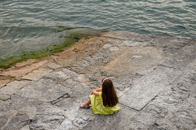 High angle view of girl with long hair sitting on footpath by lake