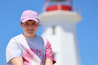 Portrait of smiling girl against sky with lighthouse blurred in background 