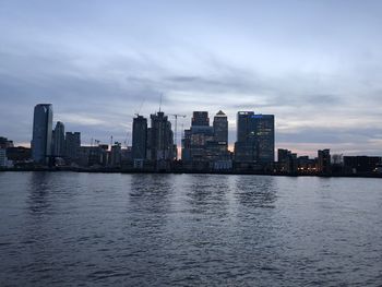 Sea by buildings against sky at dusk