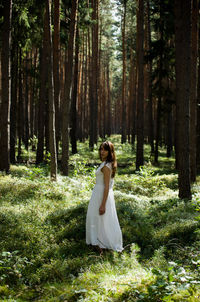 Full length portrait of young woman standing on field in forest