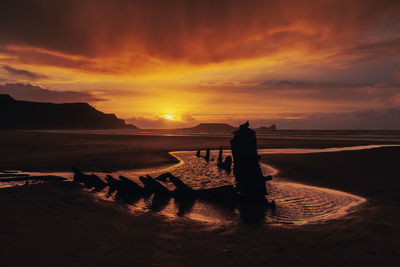 Silhouette shipwreck at beach against sky during sunset