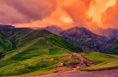 Scenic view of green mountains against dramatic sky during sunset