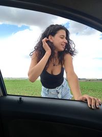 Young woman looking away while standing by car outdoors