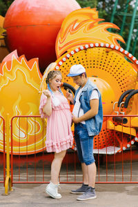 Funny future parents eat lollipops and show each other their bellies at an amusement park