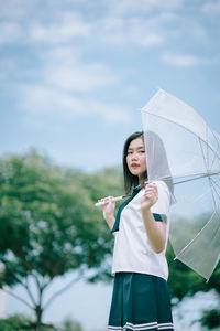 Portrait of young woman with umbrella standing against sky