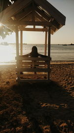 Rear view of woman sitting on beach against clear sky