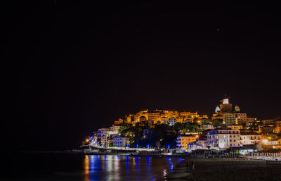 Beach by illuminated buildings at night