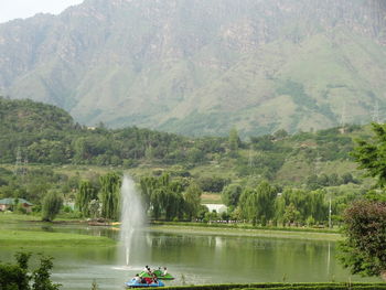 People on riverbank by mountains against sky