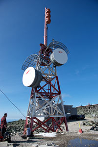 Low angle view of men by communications tower against clear blue sky