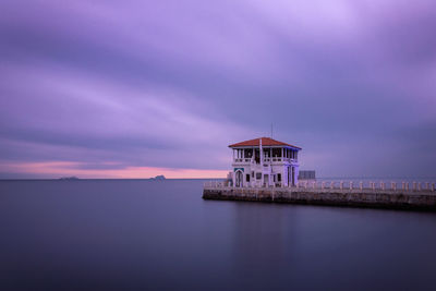 Building by sea against sky at sunset