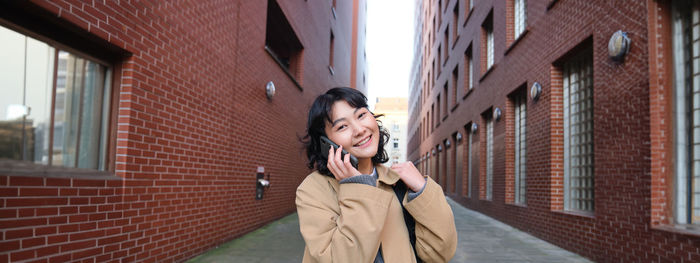 Portrait of young woman standing against building