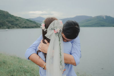 Rear view of couple standing by lake against mountains