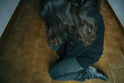 High angle view of depressed woman kneeling on tiled floor