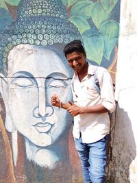 Portrait of smiling young man standing against graffiti wall