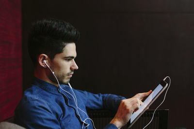 Profile of young businessman with earphones using digital tablet in front of black background