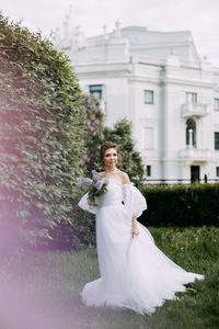 Young woman standing against white wall with plants in foreground