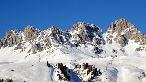 Low angle view of snowcapped mountains against clear blue sky