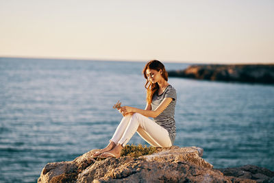 Woman sitting on rock by sea against sky