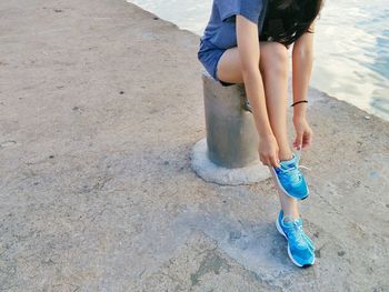 Low section of woman tying shoelace while sitting on bollard