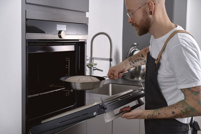 Man putting proofed sourdough bread into oven