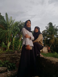 Portrait of smiling young woman standing against plants and trees
