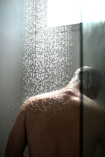 Rear view of man taking shower in bathroom