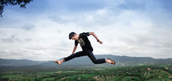 Side view of young man jumping against mountain