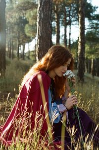 Woman holding umbrella on field in forest