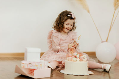 A cute little girl is sitting on the floor with a cake and gifts on her birthday 