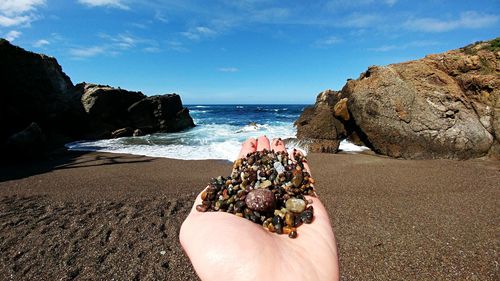 Close-up of hands on beach against sky