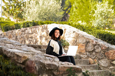 Young woman sitting on rock with laptop