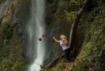 Woman throwing autumn leaves against waterfall