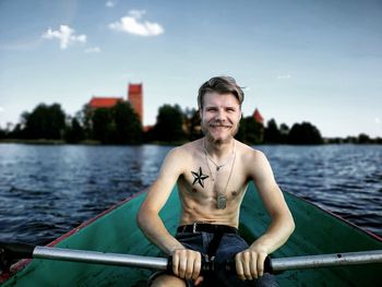 Portrait of smiling shirtless young man rowing boat in river