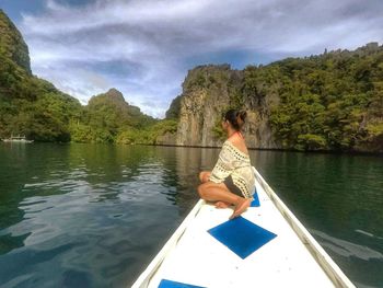 Rear view of man sitting on lake against sky